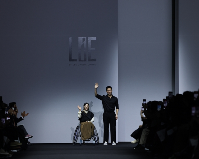 LIE’s Lee Chung-chung (right) and a model in a wheelchair wave at the fall-winter 2024 Seoul Fashion Week at Dongdaemun Design Plaza in February. (Seoul City)